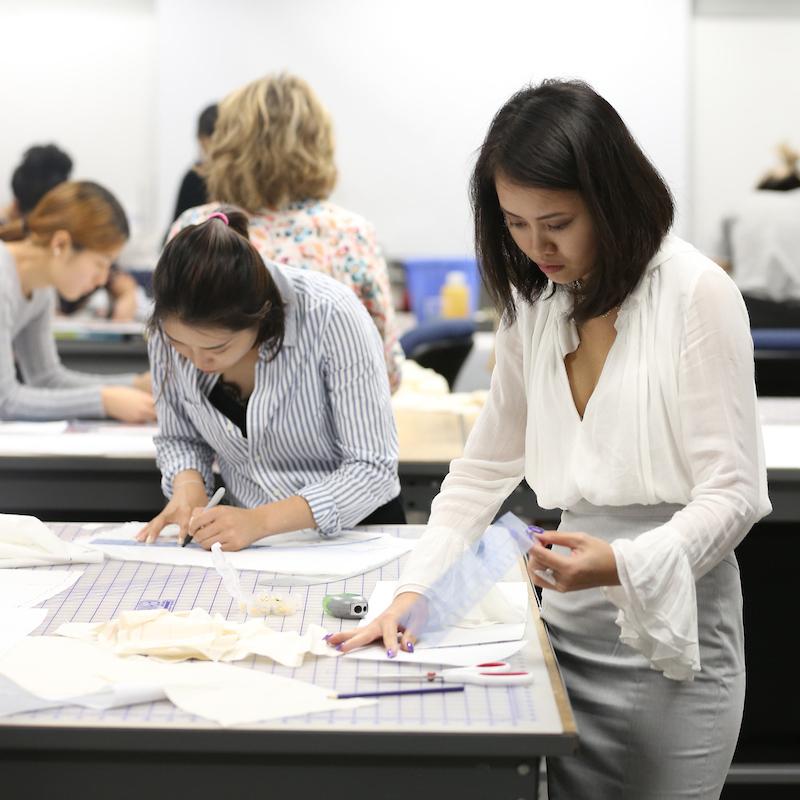 A group of students work on projects in the fashion design workroom.