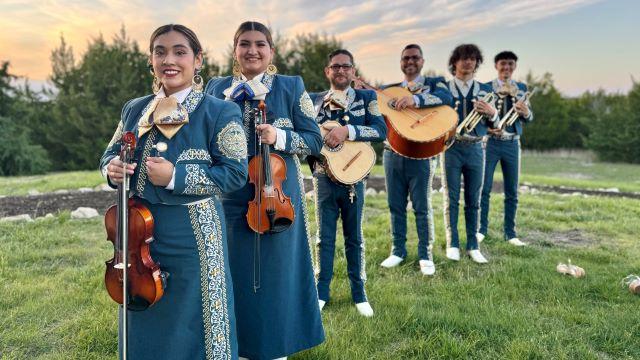 members of Mariachi Estrella standing in a line. They are holding their instruments and smiling at the camera. All are wearing traditional clothing. 